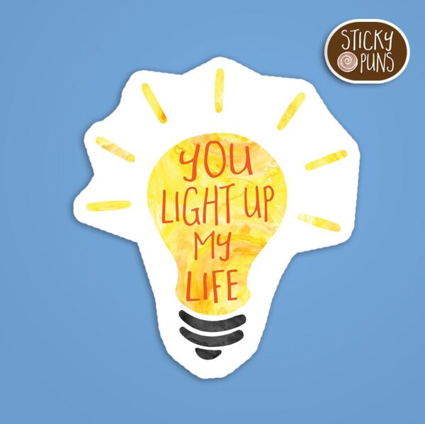 A pun sticker with the phrase 'You light up my life' written on a light bulb.  Sticker is on a blue background with a sticky puns logo in the top right corner.