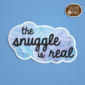 A pun sticker with the phrase 'The snuggle is real' written on a blue puffy cloud blanket.  Sticker is on a blue background with a sticky puns logo in the top right corner.