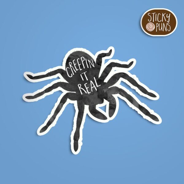 A pun sticker with the phrase 'creepin it real' featuring a spooky spider. Sticker is on a blue background with a sticky puns logo in the top right corner.