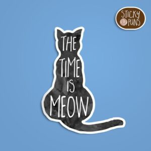 A pun sticker with the phrase 'The time is MEOW' featuring a cute cat.  Sticker is on a blue background with a sticky puns logo in the top right corner.