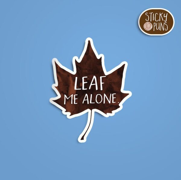 A pun sticker with the phrase 'Leaf me alone' written on a leaf, celebrating the introvert's desire for solitude. Sticker is on a blue background with a sticky puns logo in the top right corner.