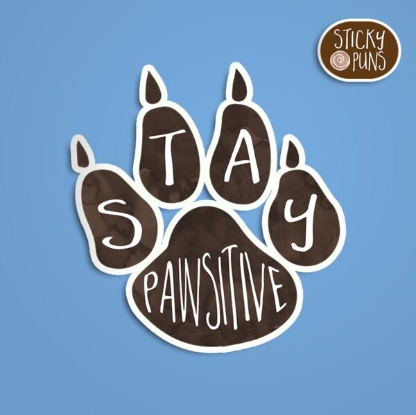 A pun sticker with the phrase 'stay pawsitive' featuring paw prints. Sticker is on a blue background with a sticky puns logo in the top right corner.