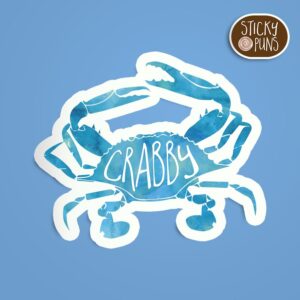 A pun sticker featuring a crab with the word 'crabby.' Sticker is on a blue background with a sticky puns logo in the top right corner.