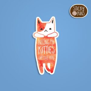 A pun sticker with the phrase 'freezing my kitties off.' Sticker is on a blue background with a sticky puns logo in the top right corner.