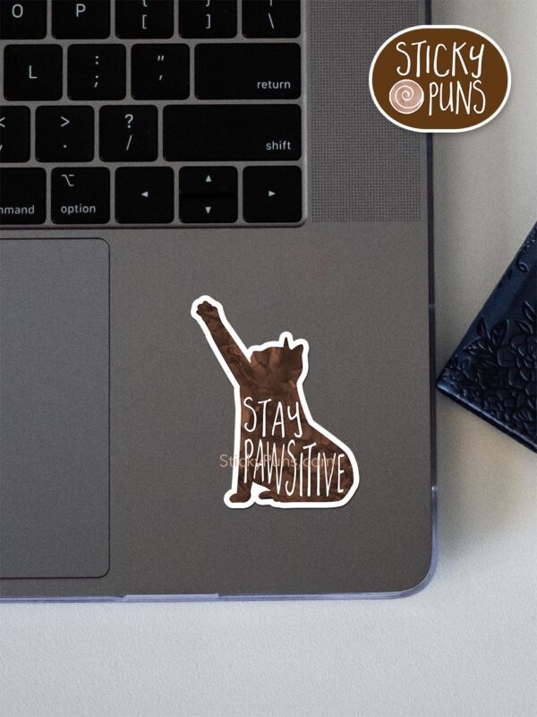 Stay PAWsitive - cute cat pun sticker shown stuck on a laptop