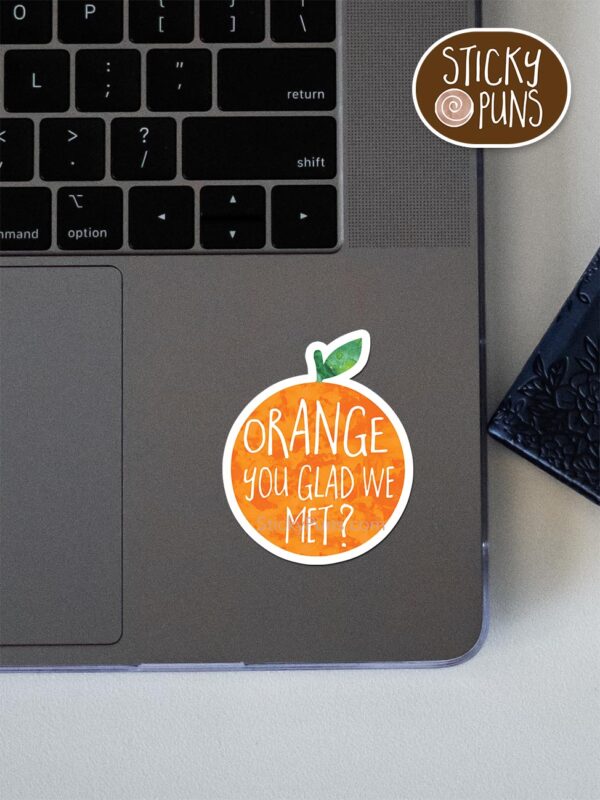 Orange You Glad We Met? pun sticker shown stuck on a laptop