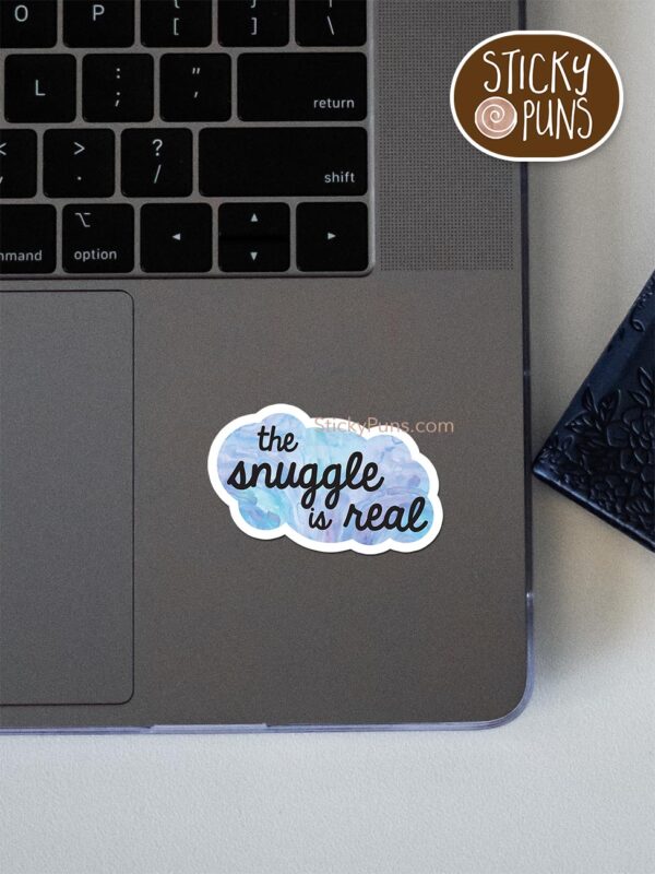 snuggle is real pun sticker shown stuck on a laptop